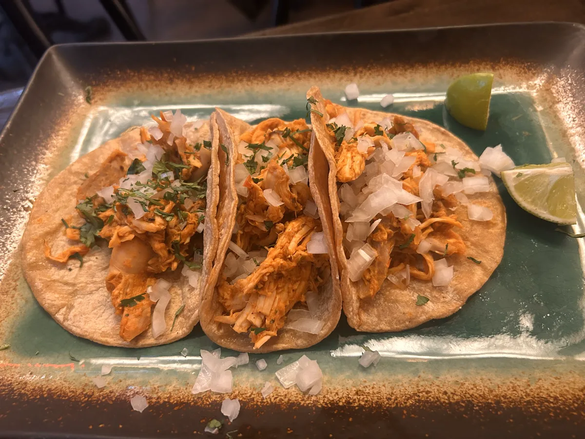 Three filled tacos on a dark plate with lime wedges